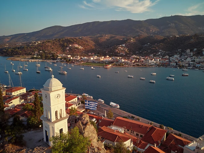 Poros island. Clock tower in old town with traditional white houses near the sea